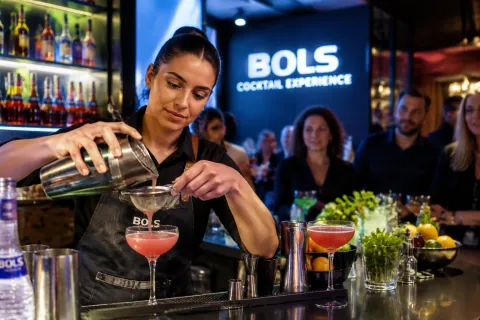 Barkeeper schenkt roze cocktail in coupeglas bij drukke Bols cocktailbar verlichting