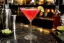 Roze Cosmopolitan in cocktailglas met limettwijf aan rand, baraccessoires op marmerblad