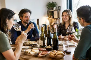 Vieren vrienden thuis wijnproeverij met glazen, wijnflessen en borrelplank