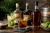 Drie flessen donkere rum met cocktailglas en mojito op houten tafel, limoen erbij