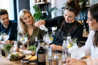 Vrouw giet tonic in gin-tonicglas terwijl deelnemers met garnituur en citroen meekijken
